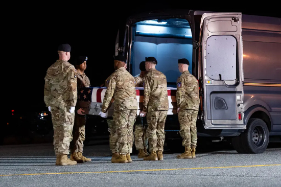 几名身着军装的人员将一具覆盖美国国旗的灵柩从厢式货车后部抬出。