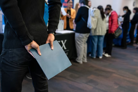 2026 年 2 月 10 日，美国西雅图市北西雅图就业资源中心招聘会现场，一名求职者手持文件夹，等待与招聘人员交流。