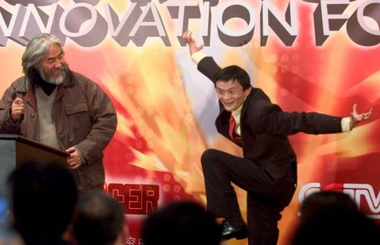 　　2005年12月8日，阿里巴巴董事长马云（右）在北京大学演讲时即兴表演制片人张继中（左）为其设计的“角色形象”。马云做出大鹏展翅动作。