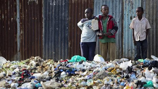 　　资料图：2010年4月7日，几名肯尼亚内罗毕当地男孩站在堆满垃圾塑料的“垃圾山”旁边。图片来源：东方IC