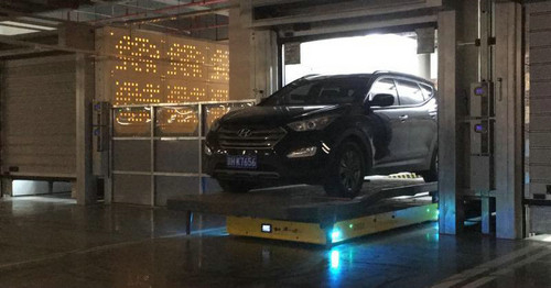 　　资料图片：汽车底下的黄色扁平长方形物件就是停车机器人，它会根据预先编写的程序把车从车库运到最近的停车位。（新加坡《联合早报》网站）