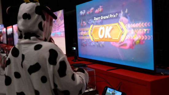 2025 年 4 月 11 日，英国伦敦，在 ExCeL 伦敦国际会展中心举办的任天堂 Switch 2 体验活动中，一名身着奶牛服装的观众正在体验《马里奥赛车世界》Switch 2 版游戏。