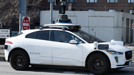 2025 年 2 月 21 日，在美国加利福尼亚州旧金山，搭载车顶传感器阵列的 Waymo 自动驾驶汽车，行驶在恩巴卡德罗街区的棕榈树与现代建筑之间。