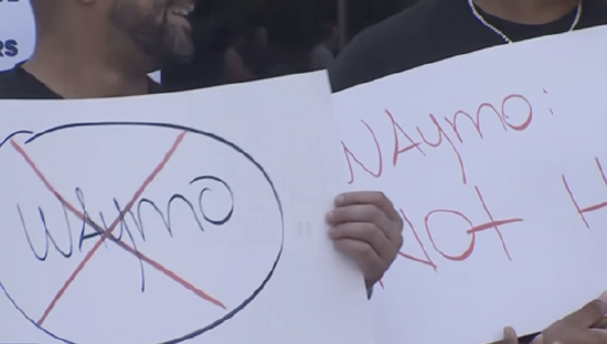 （图：纽约出租车司机在街头抗议 Waymo 自动驾驶测试，高举“Way No to Waymo”标语）