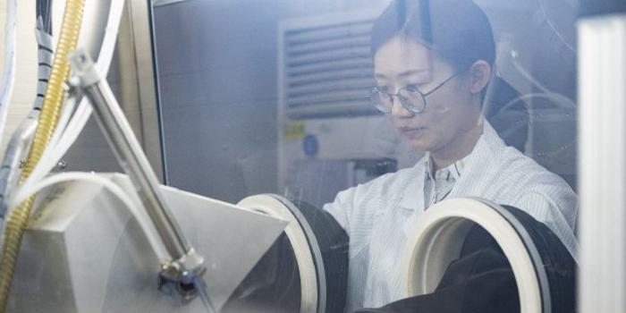 图片展示一位穿着实验室白大褂的女士，正在操作实验室设备，专注地观察着设备内部的情况。