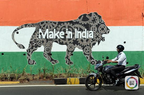 2月12日，在印度孟买，一名男子骑摩托车经过“印度制造周”宣传画。新华社/法新