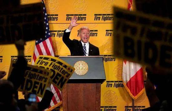  （2019年3月，拜登在国际消防员联盟大会上讲话，支持者挥舞着拜登的海报。图/Reuters）