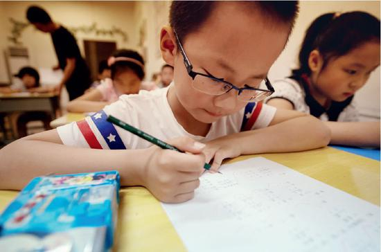  在暑期奥数补习班上解题的二年级小学生。图/新华