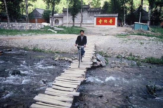 △ 1991年，山西，五台山普化寺外，一名男子在简易的木桥上骑着自行车。