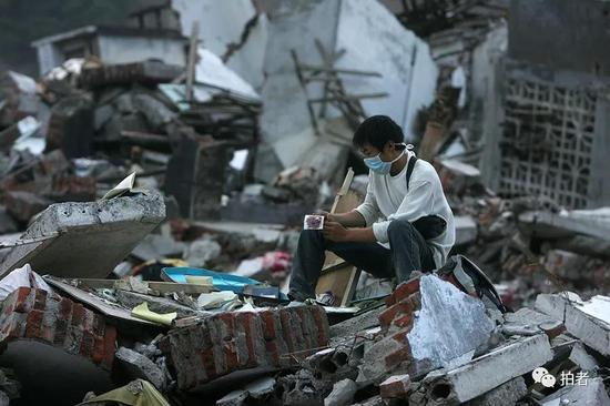 2008年6月23日，北川县城，一名抗震救灾的志愿者在废墟上寻找灾民留下的照片作为纪念。摄影/薛珺