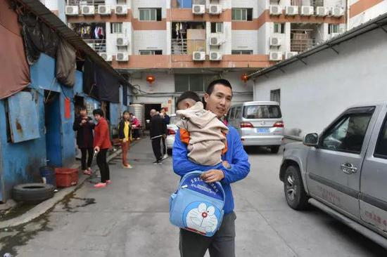 黄海龙抱着睡眼惺忪的聪聪走出工厂，准备乘坐校车去幼儿园。