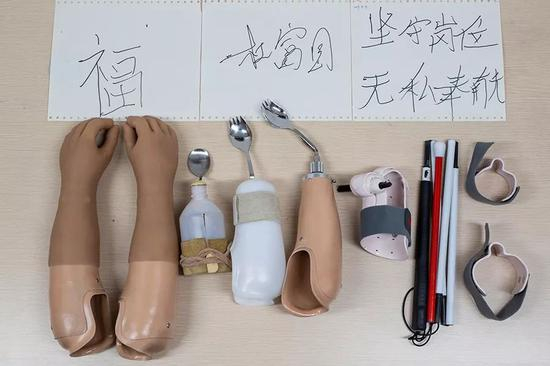 　　2019年10月24日，重庆西南医院康复楼，杜富国使用的义肢、辅助具及其用辅助具写的字。从左至右：美容义肢、第一代吃饭辅助具、第二代吃饭辅助具、第三代吃饭辅助具、写字辅助具和盲杖辅助具。新京报记者 李凯祥 摄
