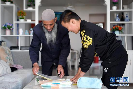在甘肃省临夏回族自治州东乡族自治县城南区易地扶贫搬迁安置小区，白银中（左）在家帮孙子白义收拾书本（8月5日摄）。新华社记者 范培珅 摄