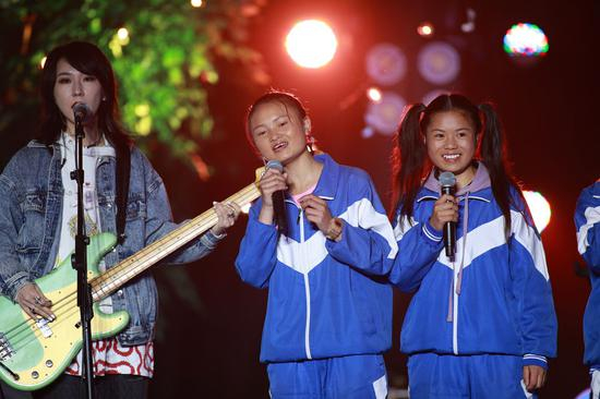 “遇”乐队吉他手李美银（中）和鼓手罗丽欣（右）在“海嘎少年的夏天”音乐会上和新裤子乐队一起演出（2020年8月19日摄）。当晚，在海拔2400米的贵州韭菜坪山腰上的六盘水市钟山区大湾镇海嘎小学，由海嘎小学的同学组成的“遇”乐队、“未知少年”乐队和颇受年轻人喜欢的摇滚乐队新裤子乐队一起演出了一场名为“海嘎少年的夏天”线上音乐会。新华社记者 刘续 摄