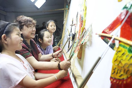  皮影艺人指导小朋友表演皮影戏。