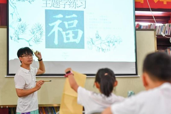 △2024年8月7日，在湖南长沙望城区月亮岛街道黄都港社区，志愿者在给小朋友上书法课。