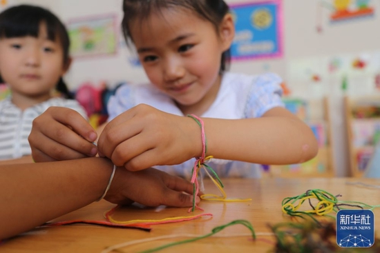 6月1日，在山东省滨州市惠民县姜楼镇幼儿园，小朋友相互系五彩绳。新华社发（王军摄）