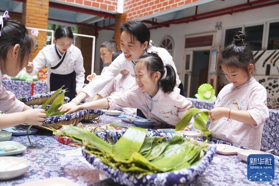 6月2日，在重庆市北碚区实验幼儿园，老师带着孩子们体验包粽子。新华社发（秦廷富摄）