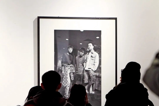 　　2017年12月，在天津举行的一场摄影展中，人们观看照片中的“魔岩三杰”张楚、何勇和窦唯。图/中新