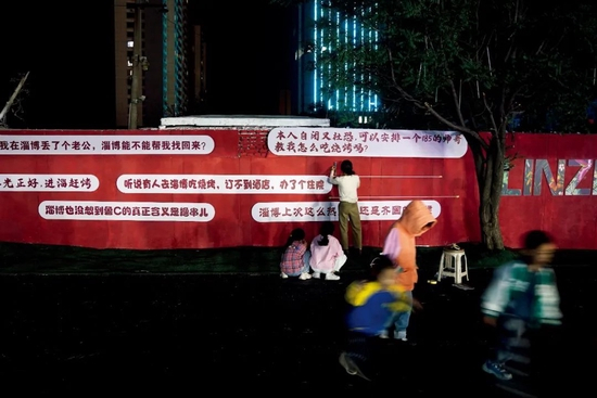  4月29日，志愿者于慧珍在给淄博的一处墙上布置宣传标语。她是一名在北京学成回到淄博的美院学生。图/视觉中国