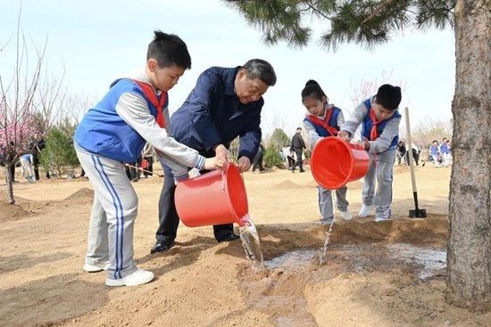2025年4月3日,习近平总书记等来到北京市丰台区永定河畔参加首都义务植树活动。这是习近平总书记同少先队员一起给刚栽下的树苗浇水。新华社记者 谢环驰 摄