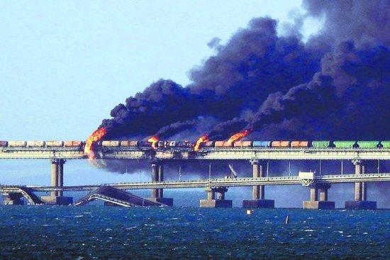 当地时间8日早晨,一辆卡车在克里米亚大桥的公路桥上发生爆炸,并导致邻近铁路桥上的火车油罐车厢被引燃。图为爆炸现场冒出浓烟,部分桥面垮塌。(法新社)