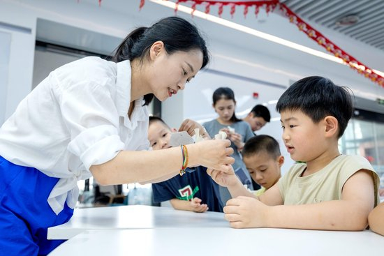 △2025年7月3日，浙江湖州长兴县龙山街道齐北社区幸福邻里中心，志愿者指导孩子们制作手工。