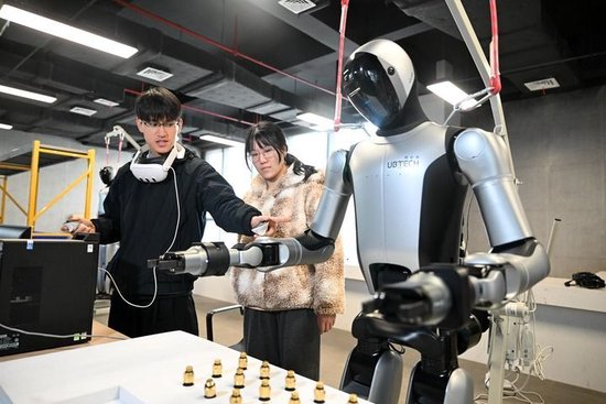 2026年2月11日，在广西柳州机器人产业园里，“00后”机器人训练师吴东波（左）和同事讨论工业人形机器人作业动作练习要领。新华社发（黎寒池摄）