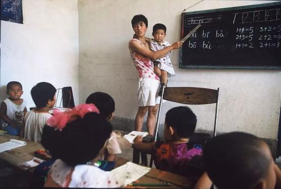 △ 1998年，山西，太原一小学教室里，一名女教师抱着孩子教学。