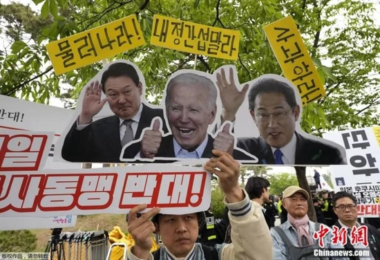  5月7日，韩国首尔，反对岸田文雄访问的集会上，一名抗议者举着美日韩三国领导人的照片。