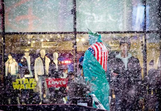 2019年12月18日，在纽约时报广场，一名打扮成“自由女神像”的街头表演者在雪中等待生意