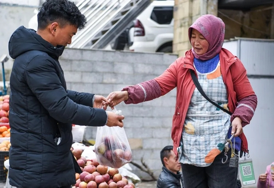 △11月30日，来自云南省昭通市的果农（右）在贵州省威宁县城售卖苹果。