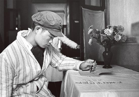 麦贤得在“八六”海战中头部负重伤，他以超人的毅力和顽强的意志，坚持战斗，直到取得胜利。经过医务人员的精心治疗和护理，他的身体逐渐恢复。图为1966年麦贤得伤愈后，右手活动还不方便，他以百折不挠的精神，练习用左手写字。 新华社 邹健东/摄