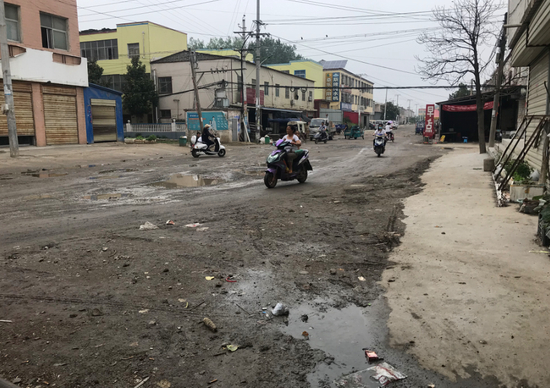 6月12日上午，八四集居民骑电动车经过卫生院前的街道。新京报记者 肖隆平 摄