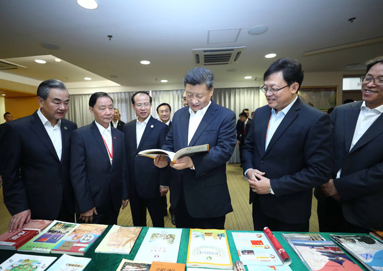 2019年12月19日，习近平在濠江中学附属英才学校图书馆仔细翻看展台上摆放的教材。