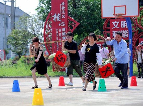 2023年6月21日，在湖州市长兴县和平镇长岗村文化礼堂前广场，当地村民正在进行挑担子绕障碍物比赛。（徐昱 摄）