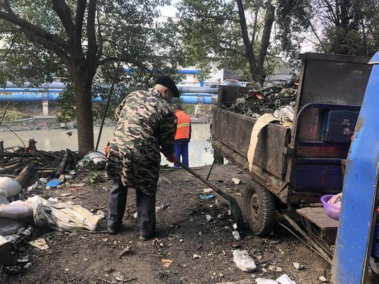  离事故现场不远处的河流沿岸，工人正在把从河里打捞上来的垃圾铲到车上，当天他们一共清理了8车垃圾。