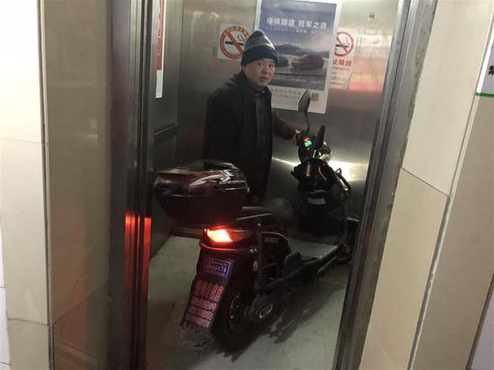 △东五小区居民董老伯正在向记者演示“梯控”的效果，电瓶车推入电梯后，电梯门顿时卡住。