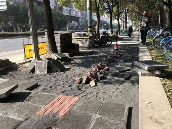 　　△天山路天山河畔小区门口的人行道上原有的小块路砖已全被挖除，正铺设新的方砖。图为行人从绿化带里借道。