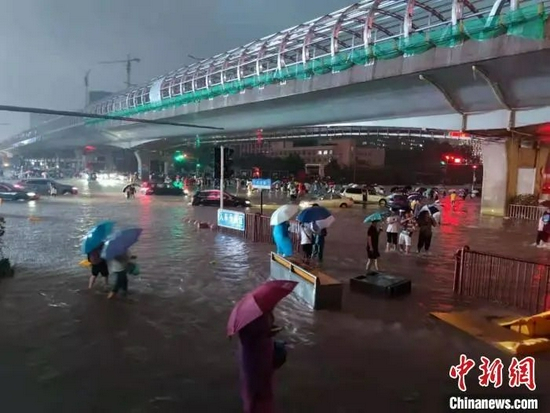 7月20日晚间，行人在路上趟水前行。　阚力 摄