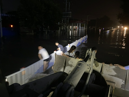 两名在水中前行的市民看到装载车过来，趴在路栏上躲避波浪。