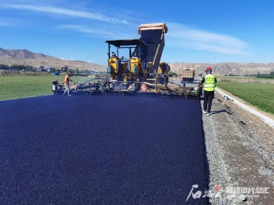 2022年6月13日，昌吉回族自治州西部南山伴行公路（二期），工人们正在摊铺沥青路面。王兵摄