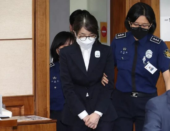  ·当地时间4月28日，金建希戴着口罩、眼镜，在狱警搀扶下入庭，胸前别着编号“4398”。（韩联社）