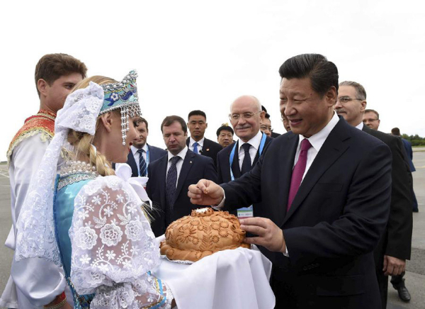 　　图 为：2015年7月8日，国家主席习近平乘坐专机抵达乌法，应俄罗斯联邦总统普京邀请，出席金砖国家领导人第七次会晤和上海合作组织成员国元首理事会第十 五次会议。这是在乌法国际机场，身穿俄罗斯民族服饰的青年按当地迎接贵宾的传统，向习近平敬献面包和盐。习近平掰下一小块面包，蘸盐品尝。