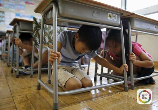 2015年9月1日 ，日本东京的一所小学举行地震演习时，学生们躲在桌子下面。新华社/路透
