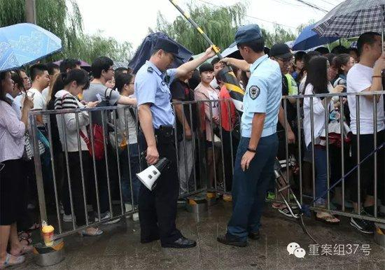 　　天通苑北地铁站入口，有小雨的早高峰，为了让打伞乘客方便通过，一位民警和一名辅警合力将“障碍物”拉高。 新京报记者 尹亚飞 摄