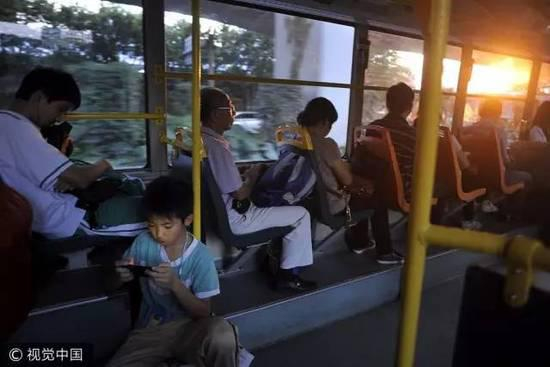 ▲广州市一辆公交车上，一位小学生坐在车内地板上玩着手机游戏。图/视觉中国