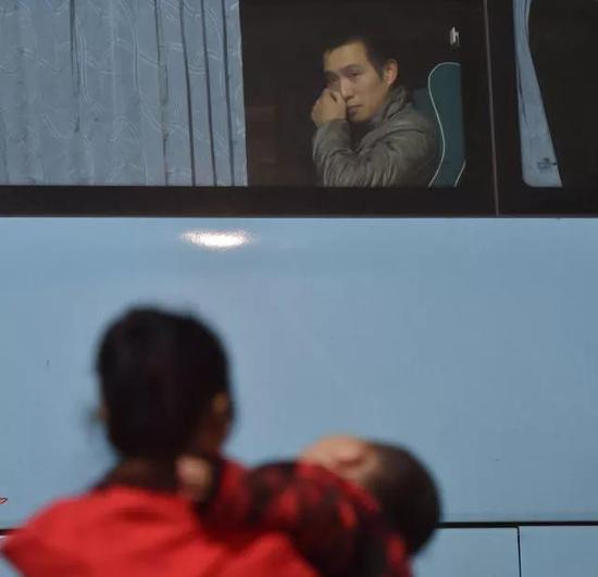 长途车上的黄海龙看着哭闹的儿子，用手擦着眼泪。