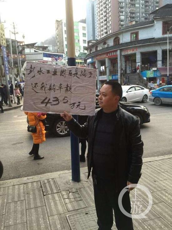 　　▲张维贵举牌维权，声称自己是相信了彭水县工业园区相关背书才买车被骗的。摄影/上游新闻记者&nbsp; 范永松