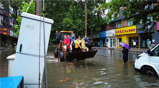 （合作路积水严重，工作人员开工程车辆转移被困群众。图源“二七发布”）